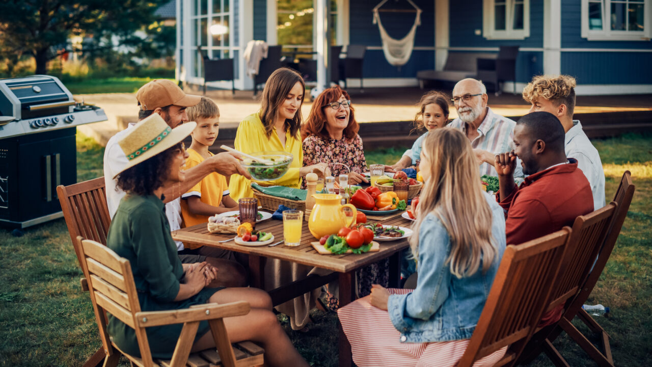 Parents, Children, Relatives and Friends Having an Open Air Vegetarian Dinner in Their Backyard. Old and Young People Talk, Chat, Have Fun, Eat and Drink. Garden Party Celebration in a Backyard.